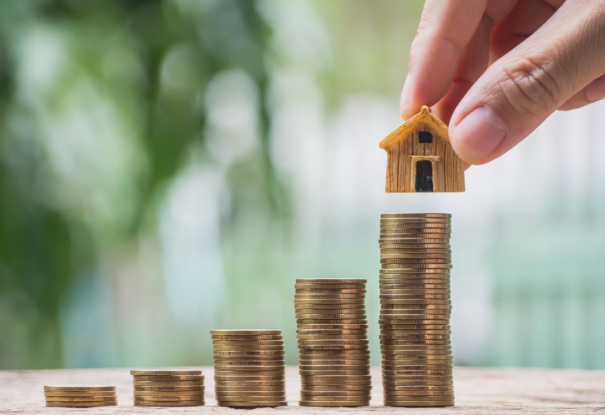 Businessman's hand putting house model on top of coins stack. Concept for loan, property ladder, financial, mortgage, real estate investment, taxes and bonus.